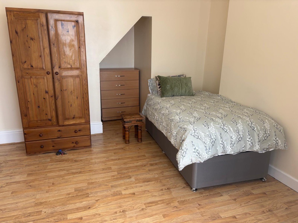 A furnished bedroom with a wardrobe, chest of drawers and a made bed
